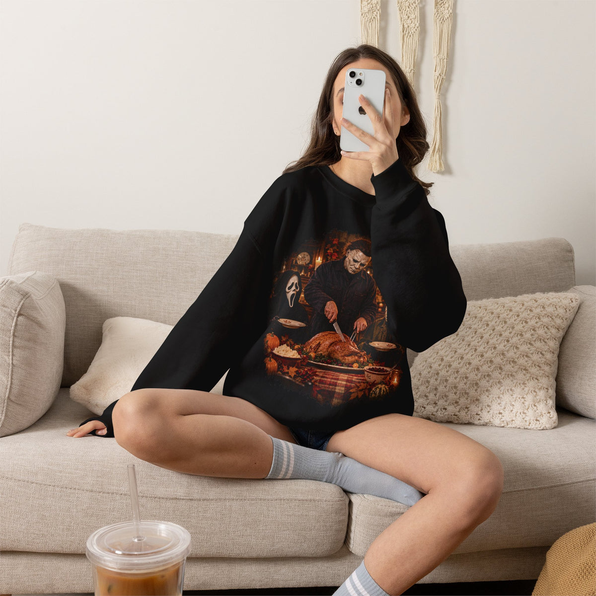 Woman wearing the Michael Myers, Ghostface and Jason Thanksgiving sweatshirt in Black, sitting on a couch
