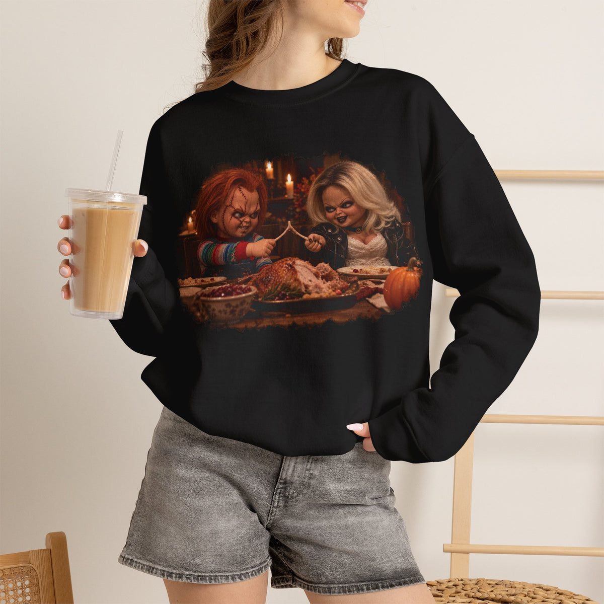 Woman wearing the Chucky & Tiffany Thanksgiving wishbone sweatshirt in Black, holding an iced coffee