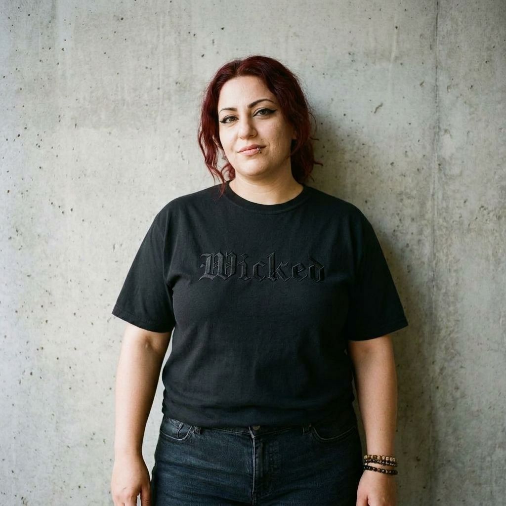 Model wearing Embroidered Wicked Gothic Text Tee – Old English Black Shirt against a cement wall