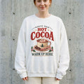 Woman wearing the Hot Cocoa Warm Up Here Christmas sweatshirt against a cement wall