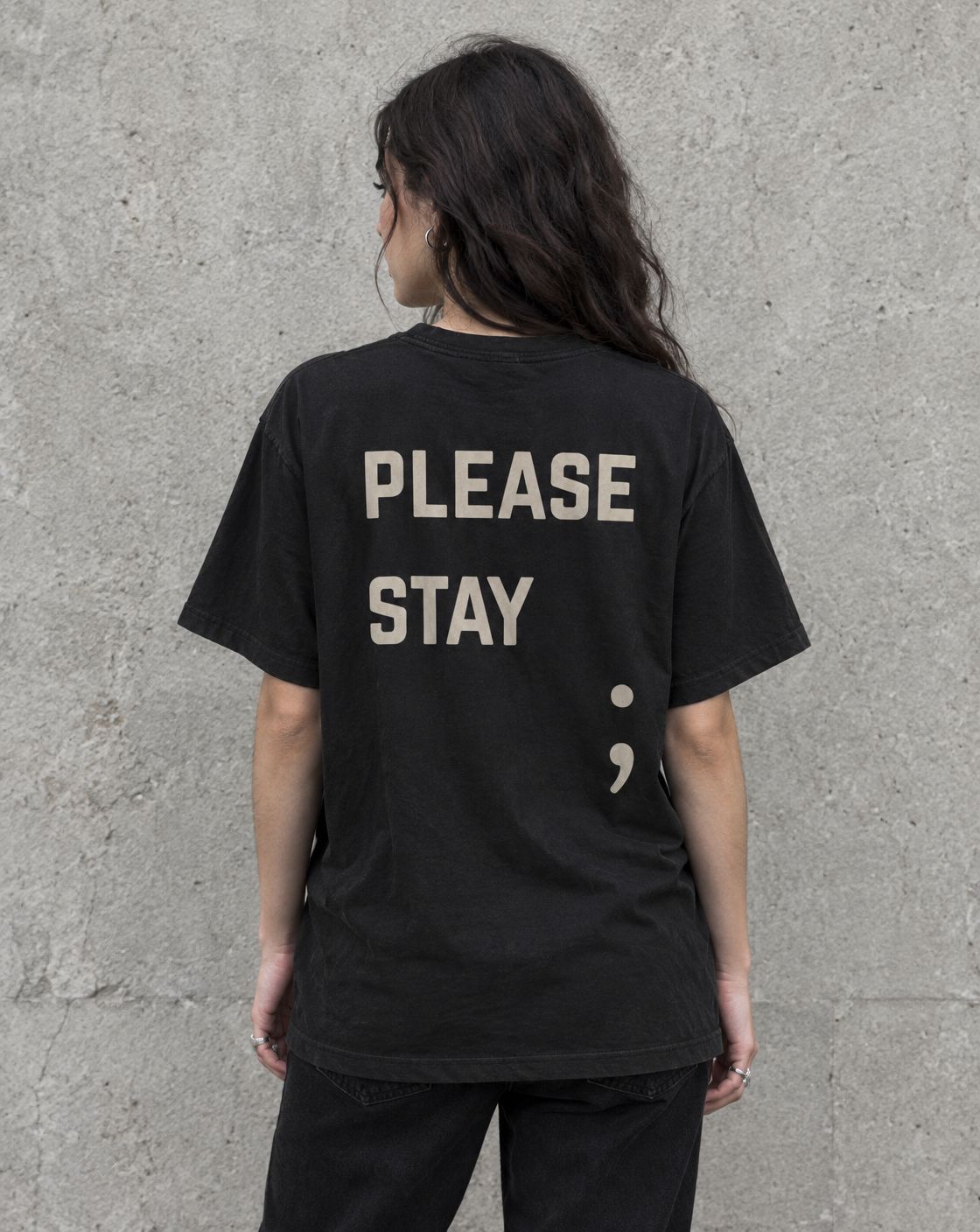 Model wearing the black Please Stay; suicide awareness t-shirt, back view