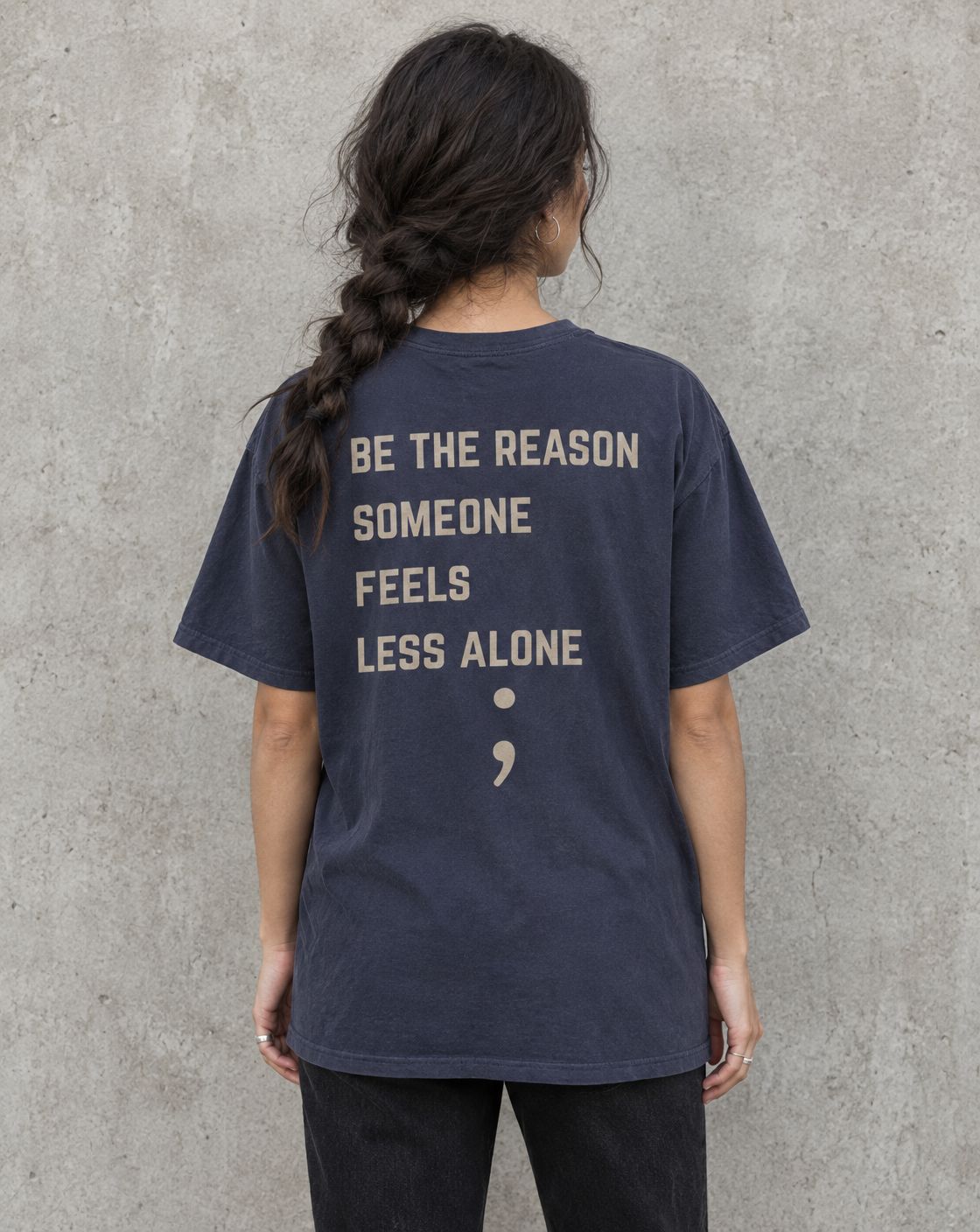 Model wearing the navy Be the Reason Someone Feels Less Alone suicide awareness t-shirt, back view