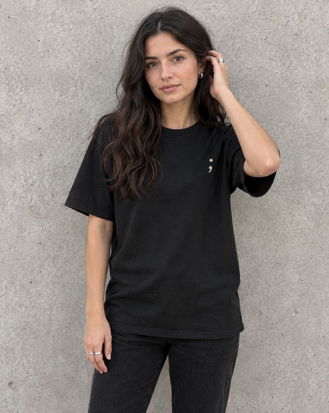 Model wearing the black Please Stay; t-shirt, front view with small semicolon