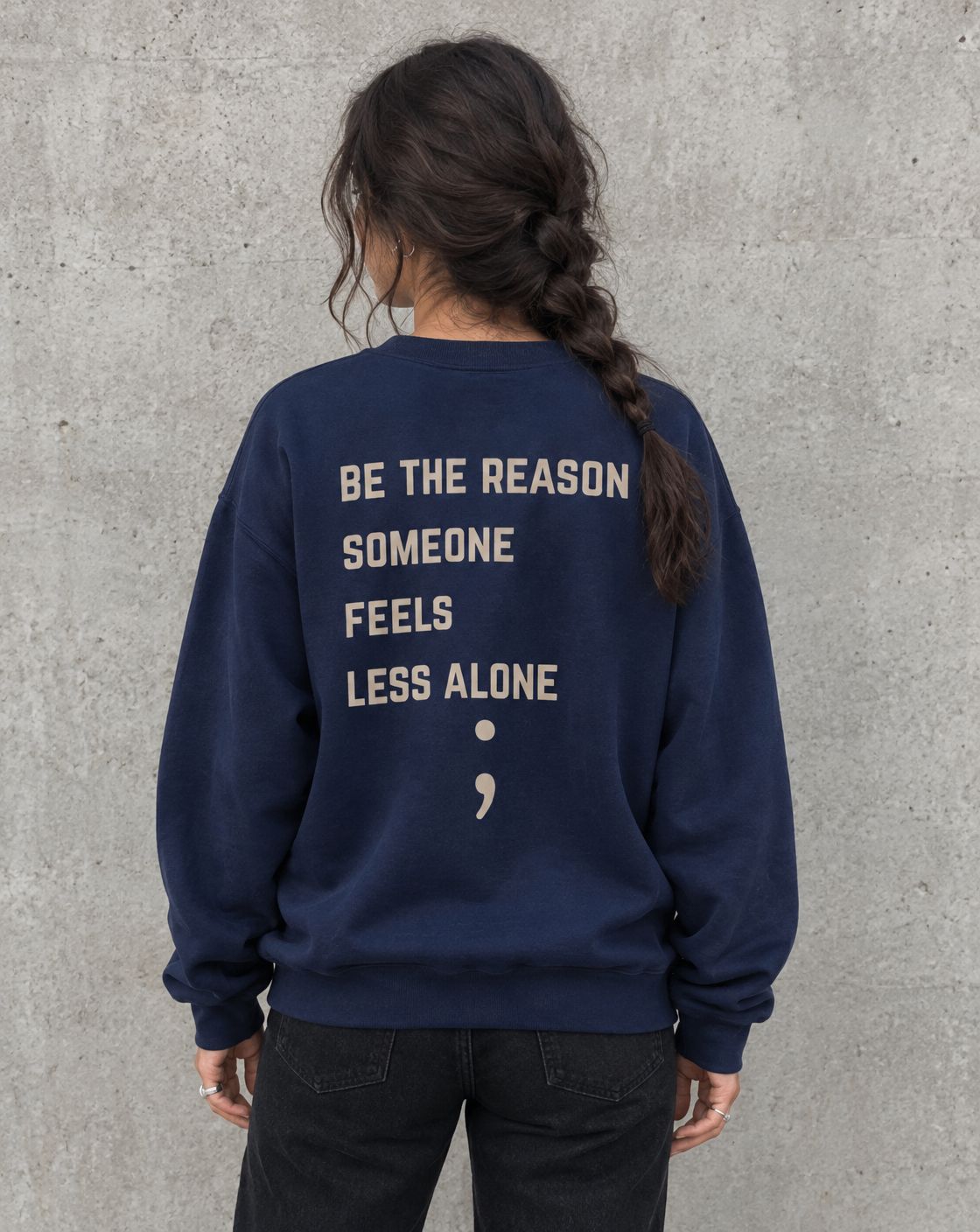 Model wearing the navy Be the Reason Someone Feels Less Alone suicide awareness crewneck sweatshirt, back view