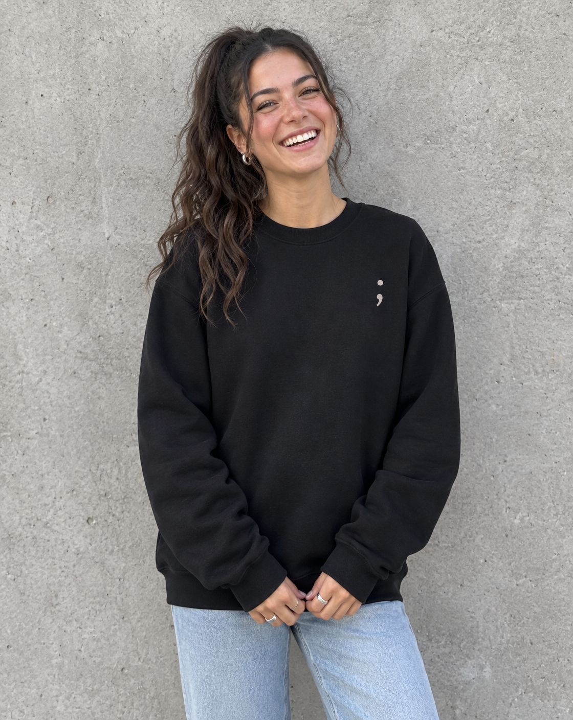 Model wearing the black Stay for Tomorrow crewneck sweatshirt, front view with small semicolon