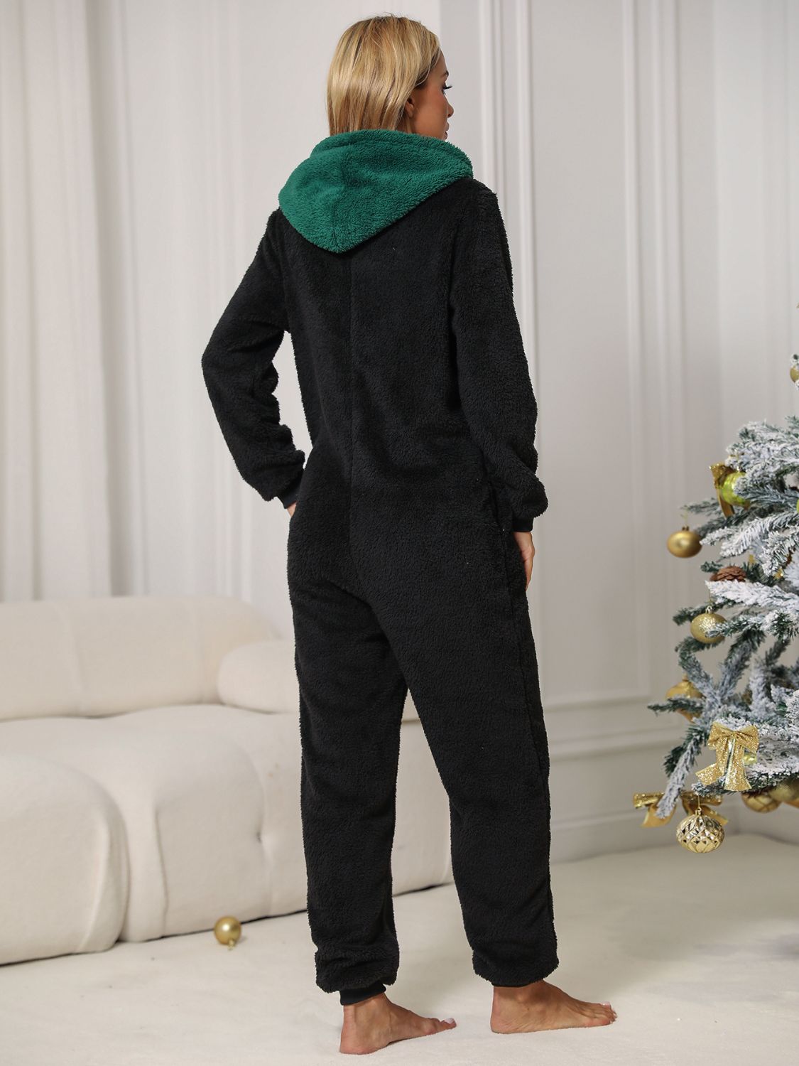 Wicked Thread Society black plush fleece lounge jumpsuit with a green hood, viewed from the back in a festive room.