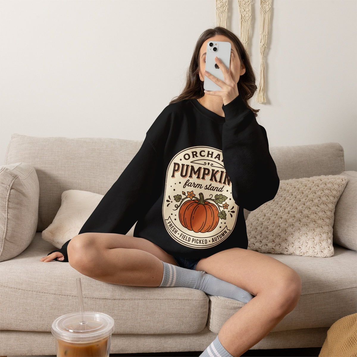 Wicked Thread Society black crewneck sweatshirt with a vintage pumpkin farmstand graphic worn by a woman on a sofa.
