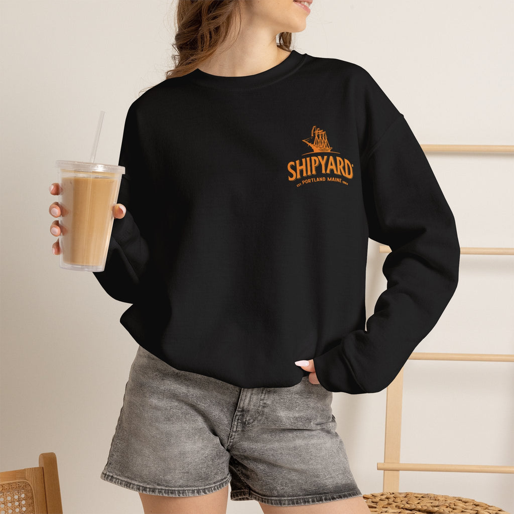 Wicked Thread Society black crewneck sweatshirt with orange Shipyard logo on chest worn by a woman holding a drink