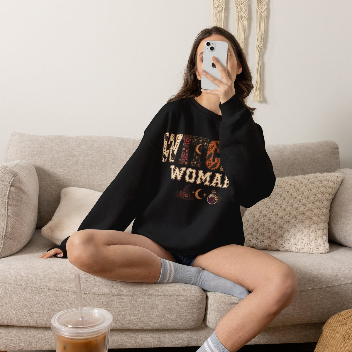 Wicked Thread Society black crewneck sweatshirt with Witchy Woman graphic print worn by a woman sitting on a sofa.