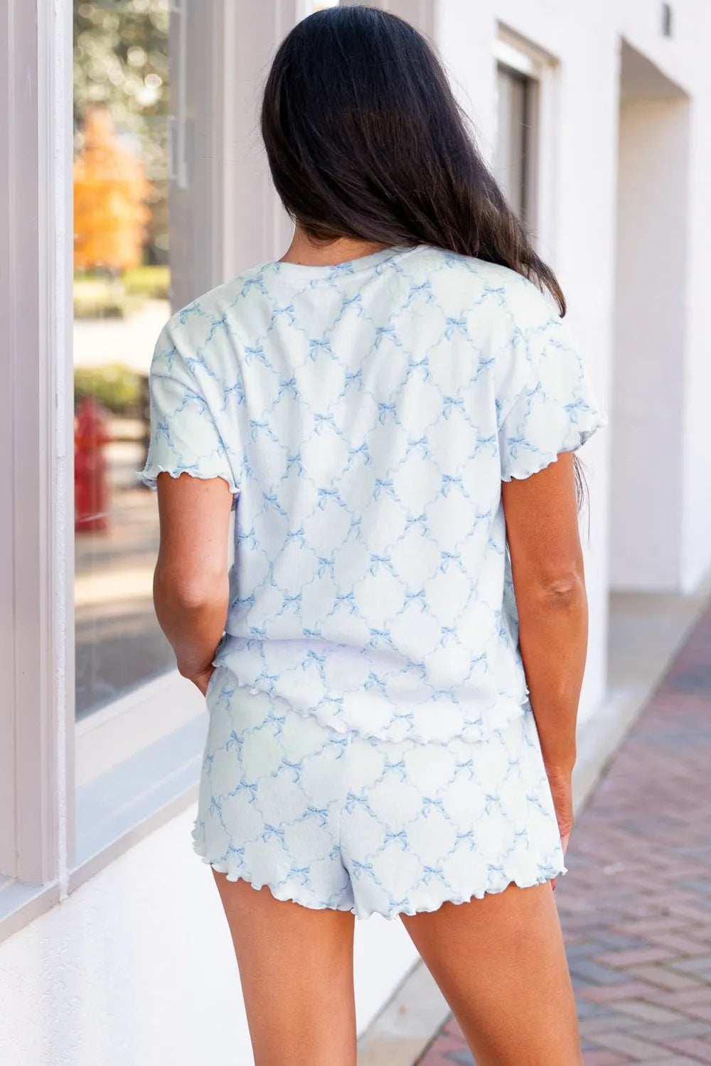 Back view of a woman wearing a Wicked Thread Society two-piece lounge set with a light blue bow print on white fabric.