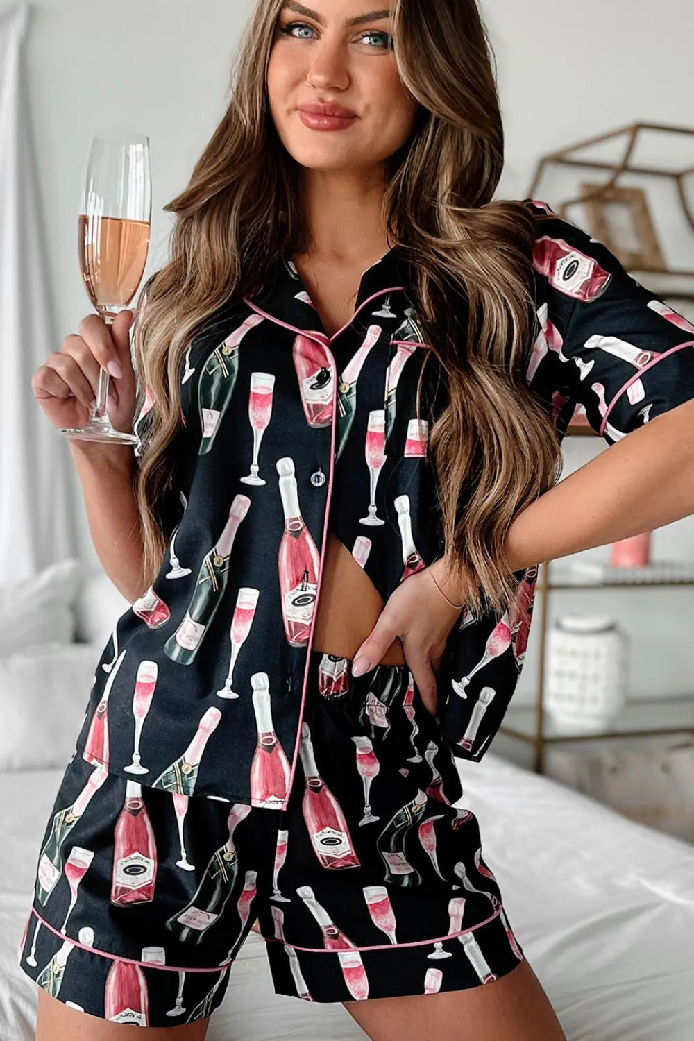 Wicked Thread Society black pajama set with champagne bottle print and pink piping worn by a woman holding a glass