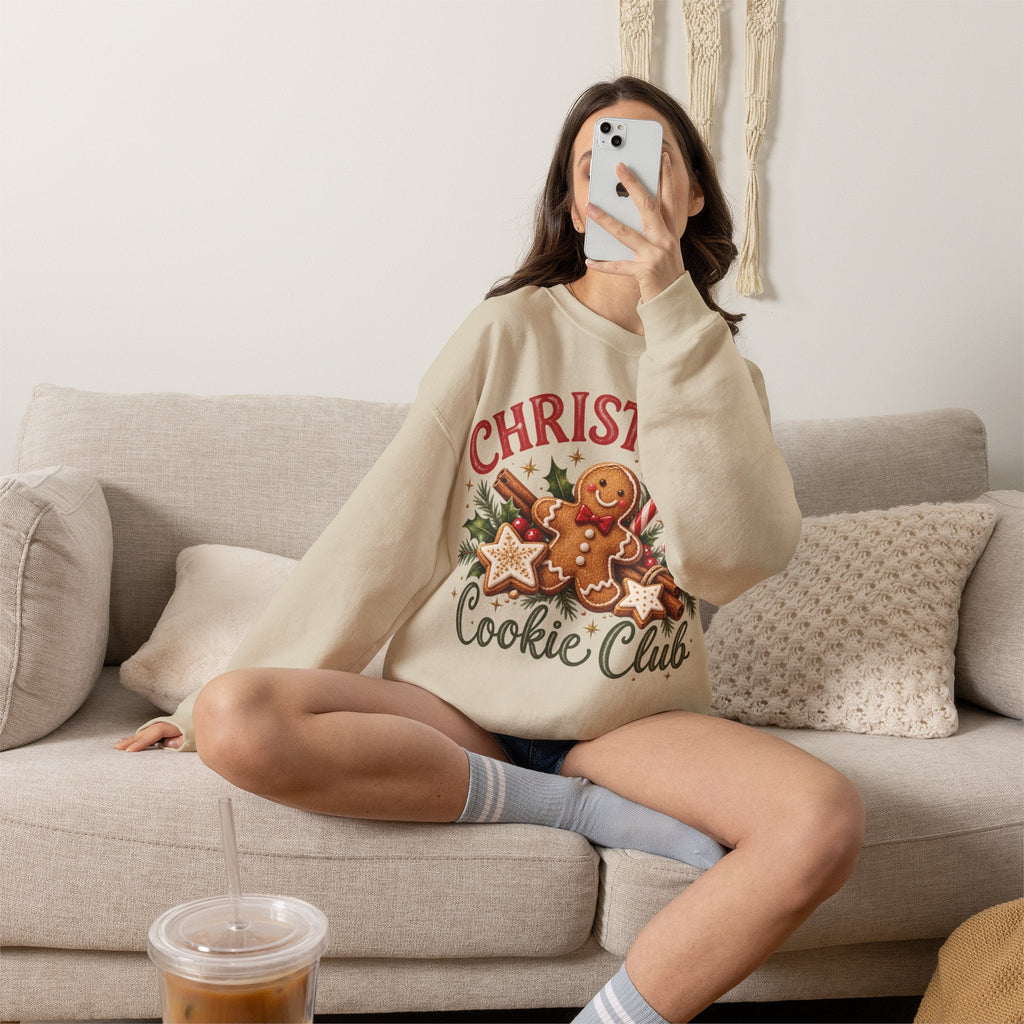 Wicked Thread Society beige crewneck sweatshirt with a gingerbread man Christmas graphic, worn by a woman on a sofa.
