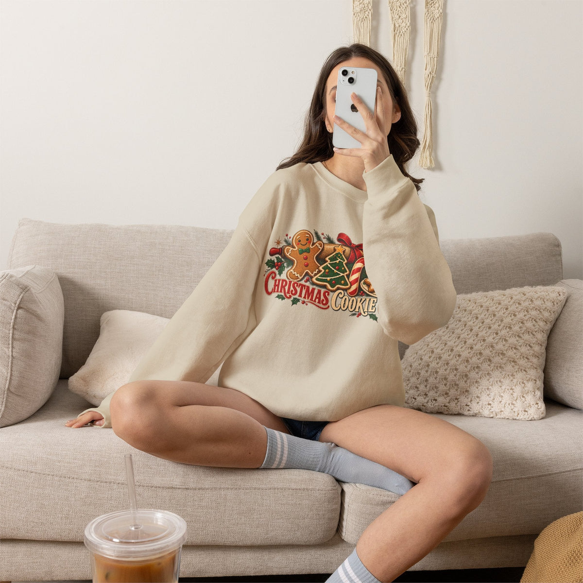 Wicked Thread Society beige crewneck sweatshirt with Christmas cookie graphic, worn by a woman sitting on a sofa.