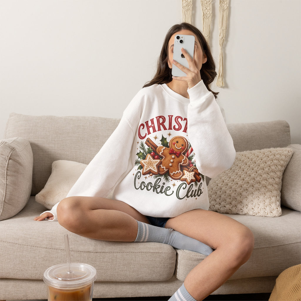 Wicked Thread Society white crewneck sweatshirt with a gingerbread man Christmas graphic worn by a woman on a sofa.