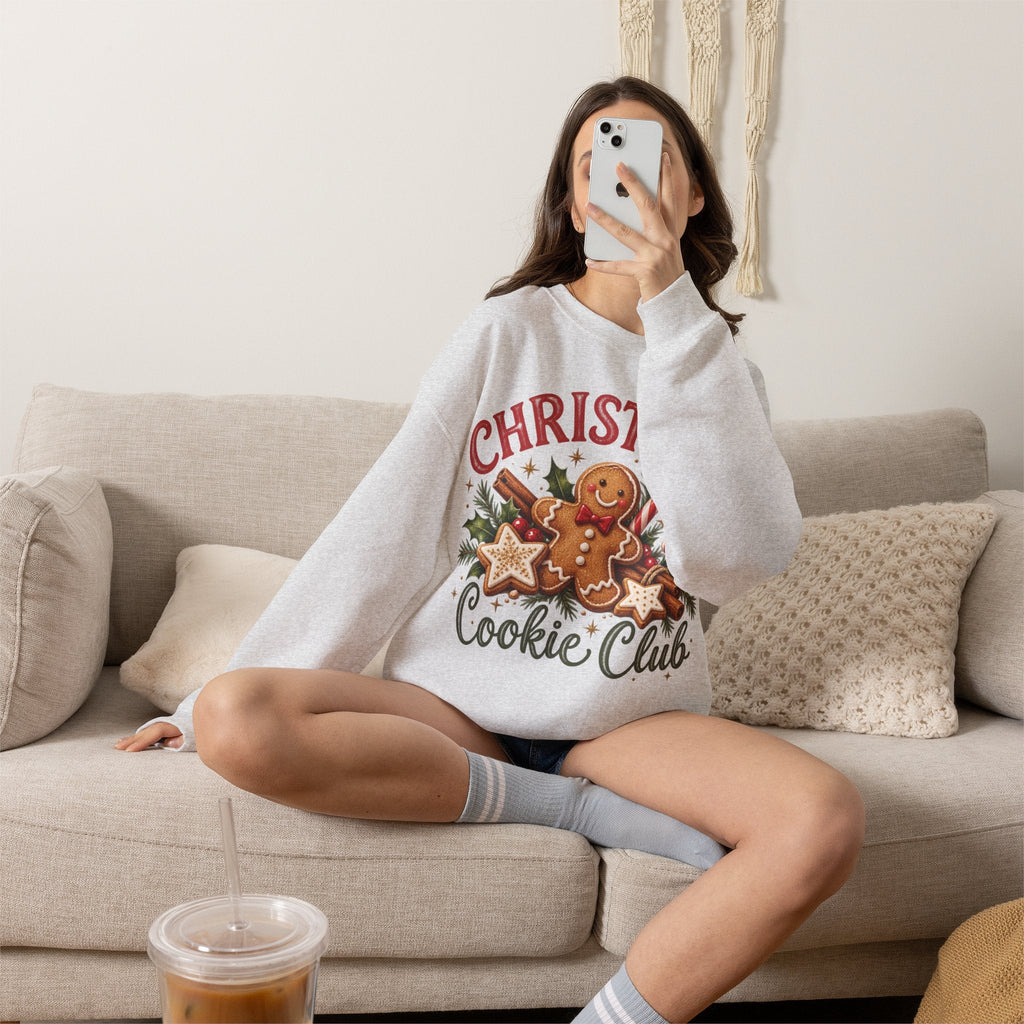 Wicked Thread Society grey crewneck sweatshirt featuring a gingerbread man graphic, worn by a woman on a beige sofa.