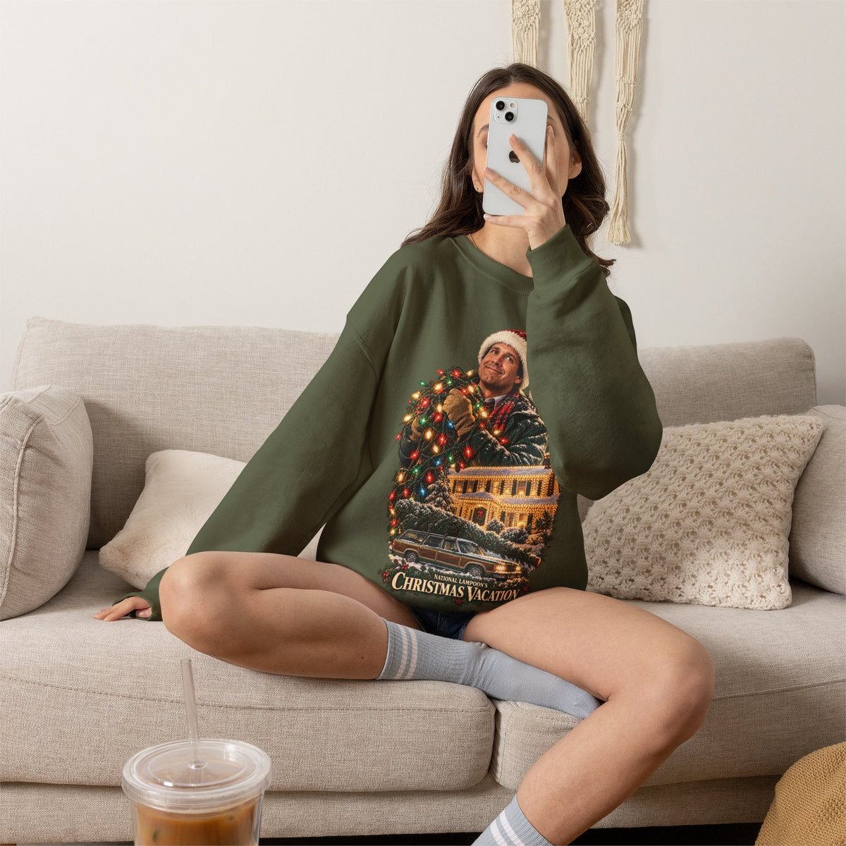 Wicked Thread Society olive green Christmas Vacation crewneck sweatshirt worn by a woman sitting on a beige sofa.