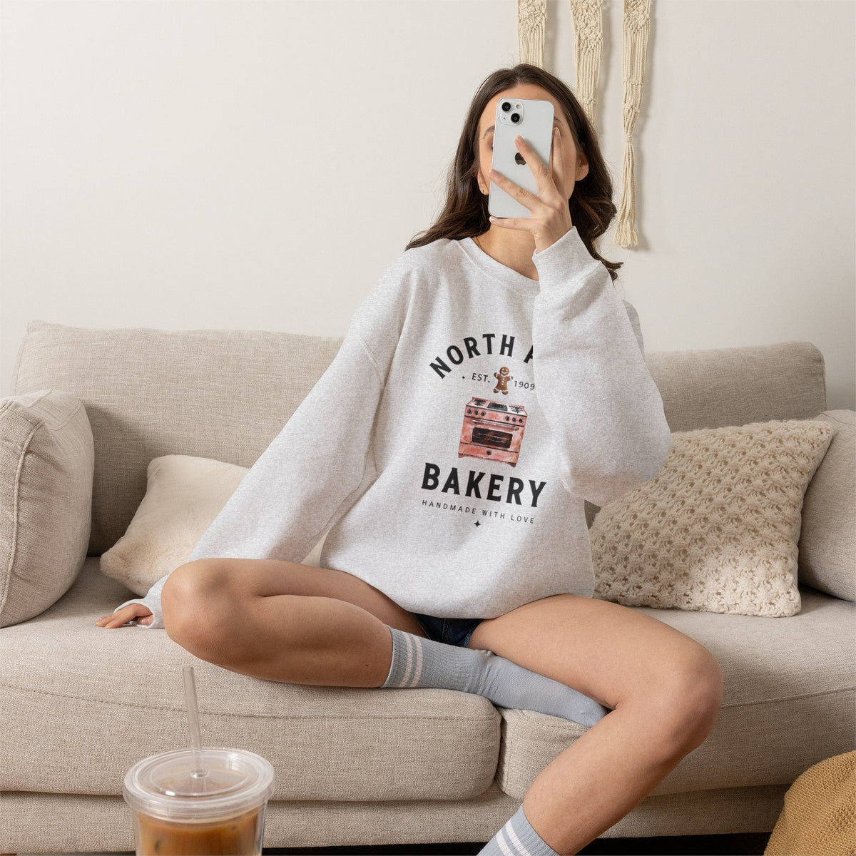 Wicked Thread Society grey crewneck sweatshirt with North Pole Bakery oven and gingerbread man graphic on a couch