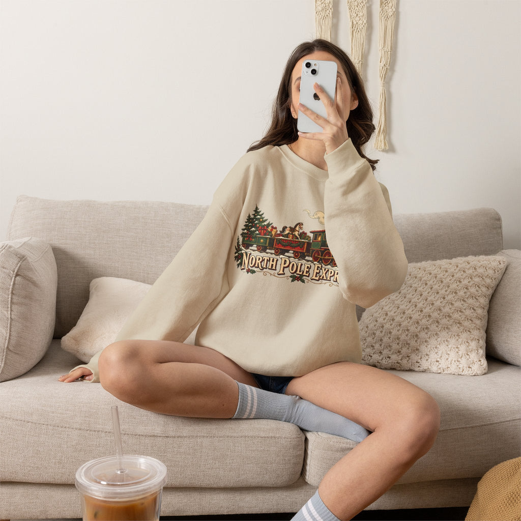 Wicked Thread Society beige crewneck sweatshirt with vintage North Pole Express train graphic worn by a woman on a sofa
