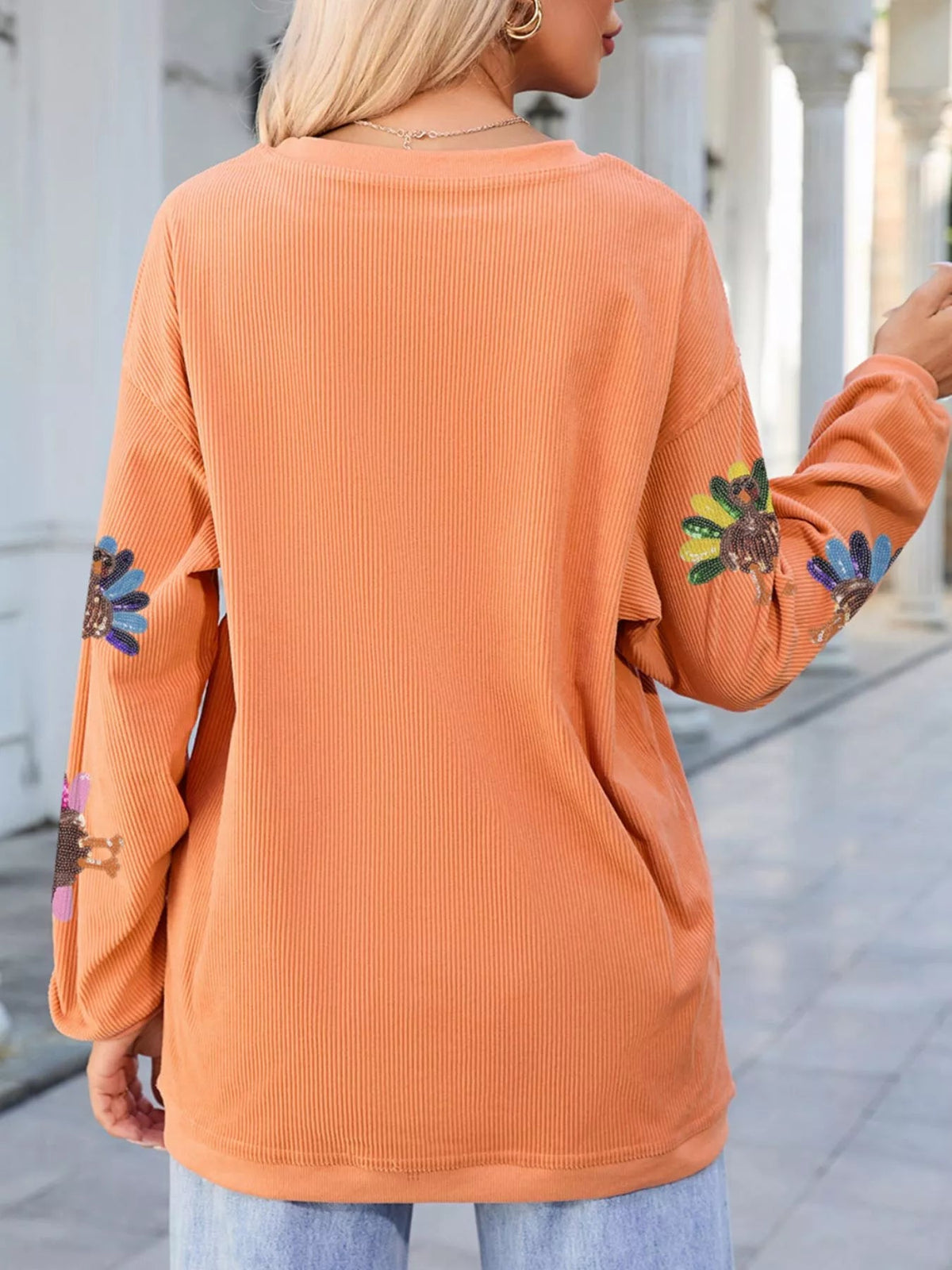 Wicked Thread Society orange corded crewneck sweater with sequin turkey graphics on sleeves, worn by a blonde woman.
