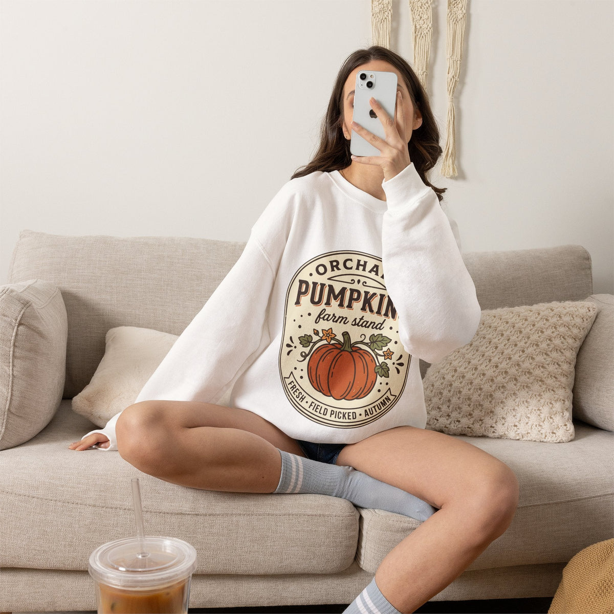 Wicked Thread Society white crewneck sweatshirt with vintage pumpkin farmstand graphic worn by a woman on a sofa