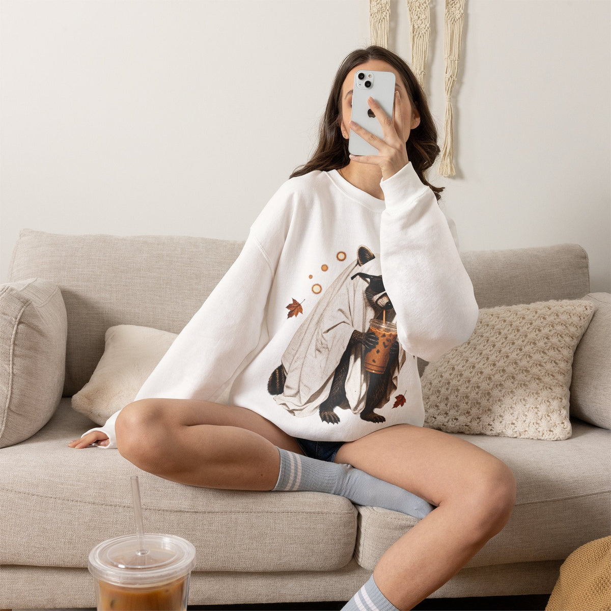 Wicked Thread Society white crewneck sweatshirt featuring a cute raccoon ghost holding boba tea on a cozy sofa.