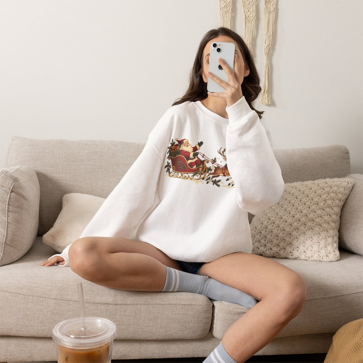 Wicked Thread Society white crewneck sweatshirt with vintage Santa sleigh and reindeer print worn by a woman on a sofa