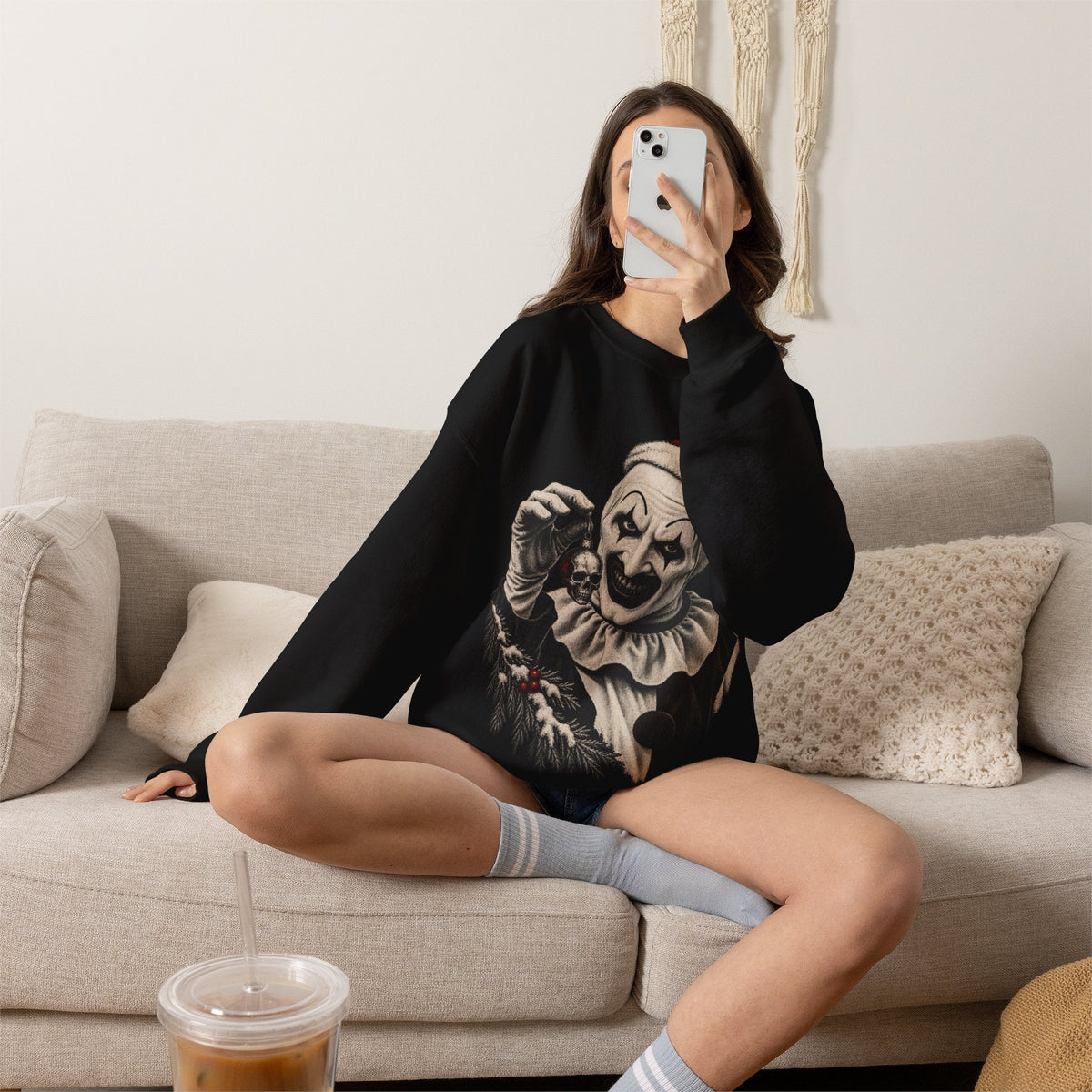 Wicked Thread Society black crewneck sweatshirt featuring Art the Clown in a Santa hat, worn by a woman on a sofa.