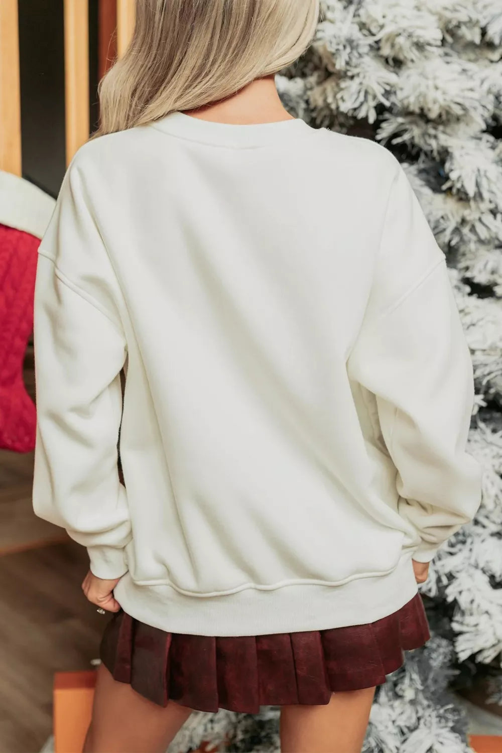 Back view of a woman wearing a Wicked Thread Society white loose drop shoulder Christmas sweatshirt with a pleated skirt