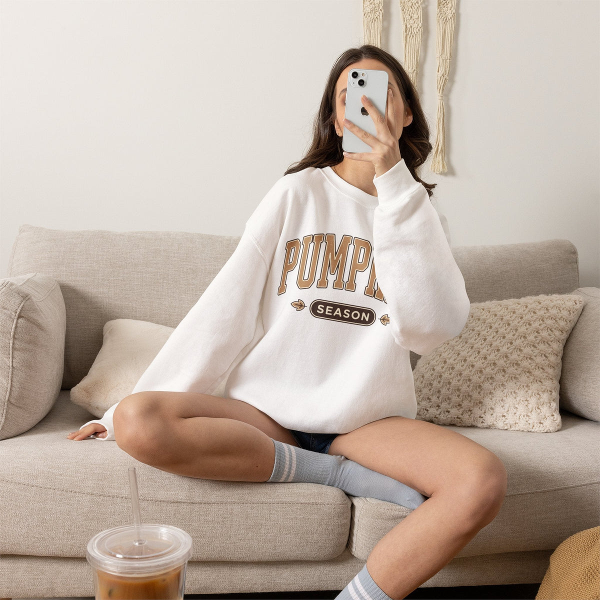 Wicked Thread Society white crewneck sweatshirt with Pumpkin Season graphic worn by a woman sitting on a beige sofa.