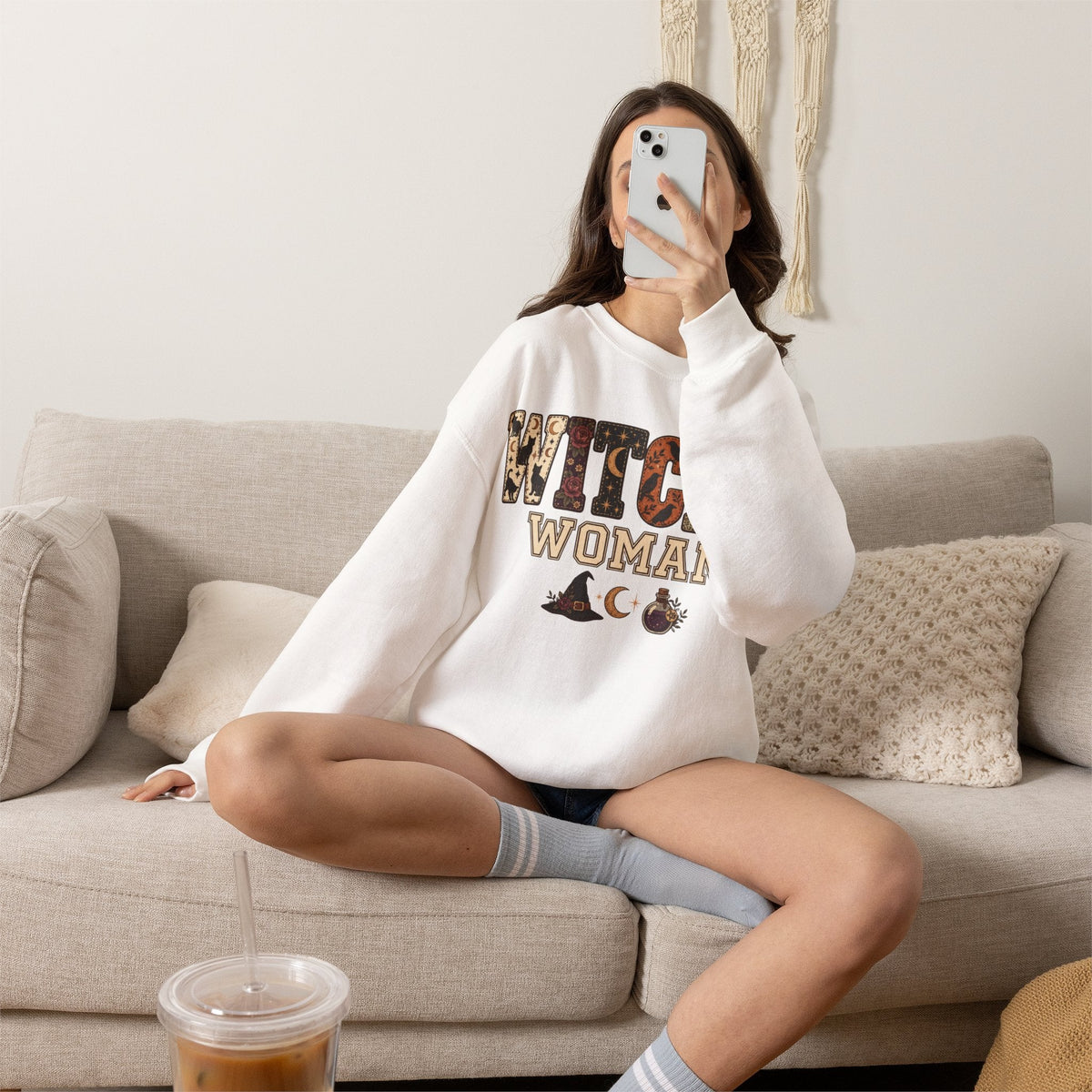 Wicked Thread Society white crewneck sweatshirt with Witchy Woman graphic print worn by a woman on a beige sofa